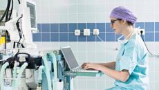 Healthcare worker in scrubs using a laptop on cardiogram machine