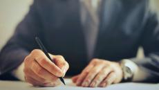 The hands of an executive in a suit are signing a document with a pen.