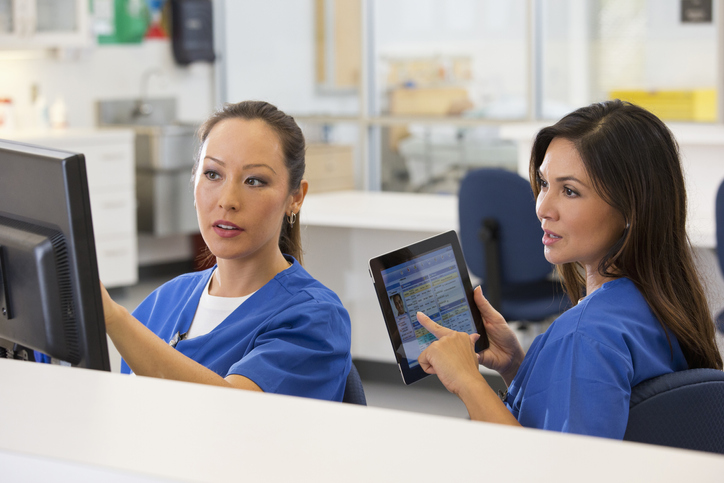 Healthcare worker with tablet looking at screen another worker is pointing at