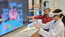 A medical student wearing a VR headset is learning the parts of the heart while being assisted by an instructor