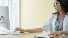 Doctor with glasses sits at a computer searching for answers.